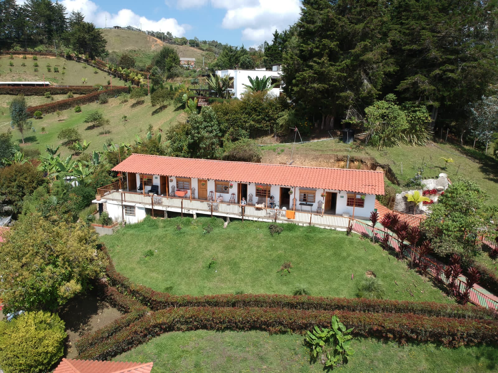 Vista aérea del hogar campestre: un edificio alargado de techo de teja rodeado de jardines, setos y colinas verdes