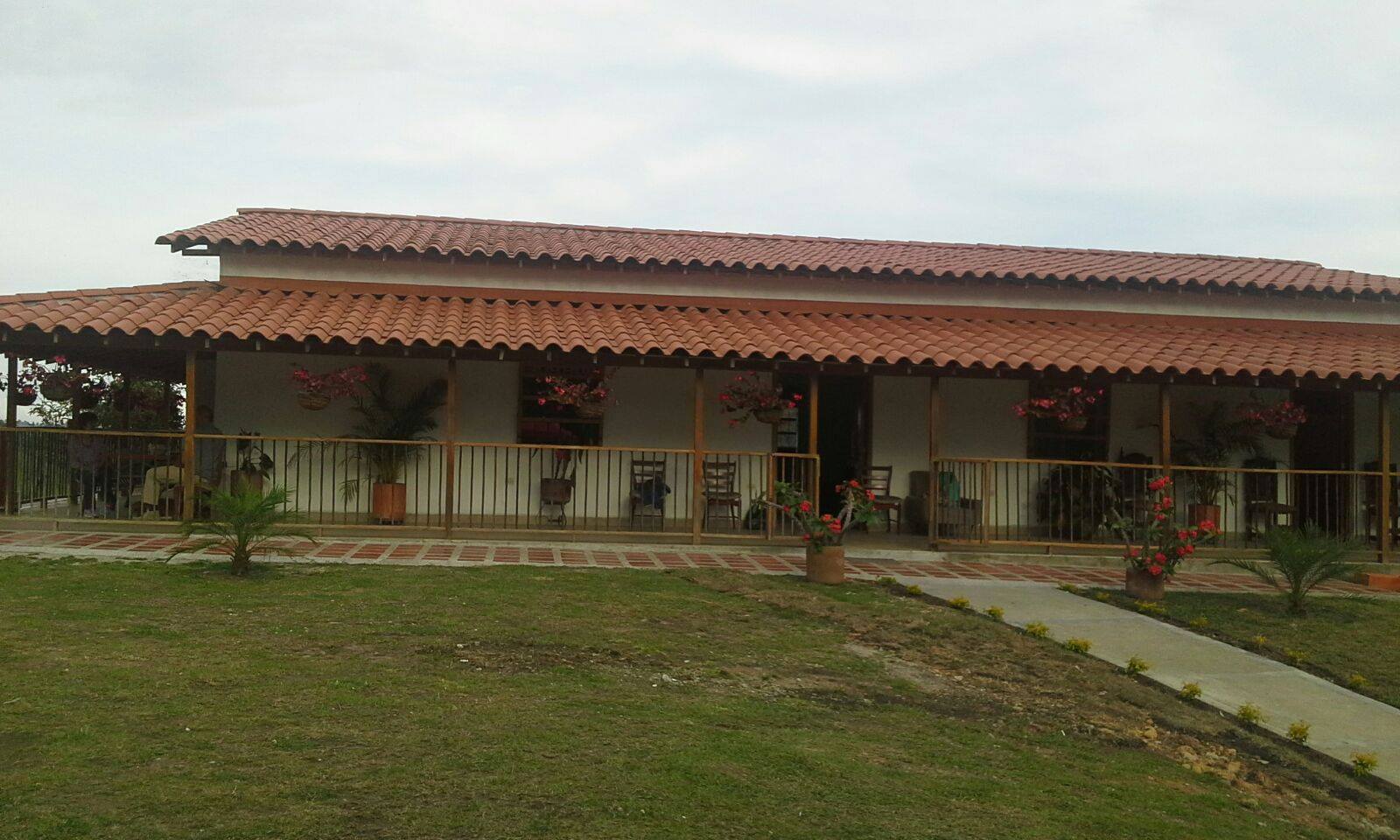Fachada del hogar con techo de teja, corredor con barandas de madera y macetas de flores frente a un prado
