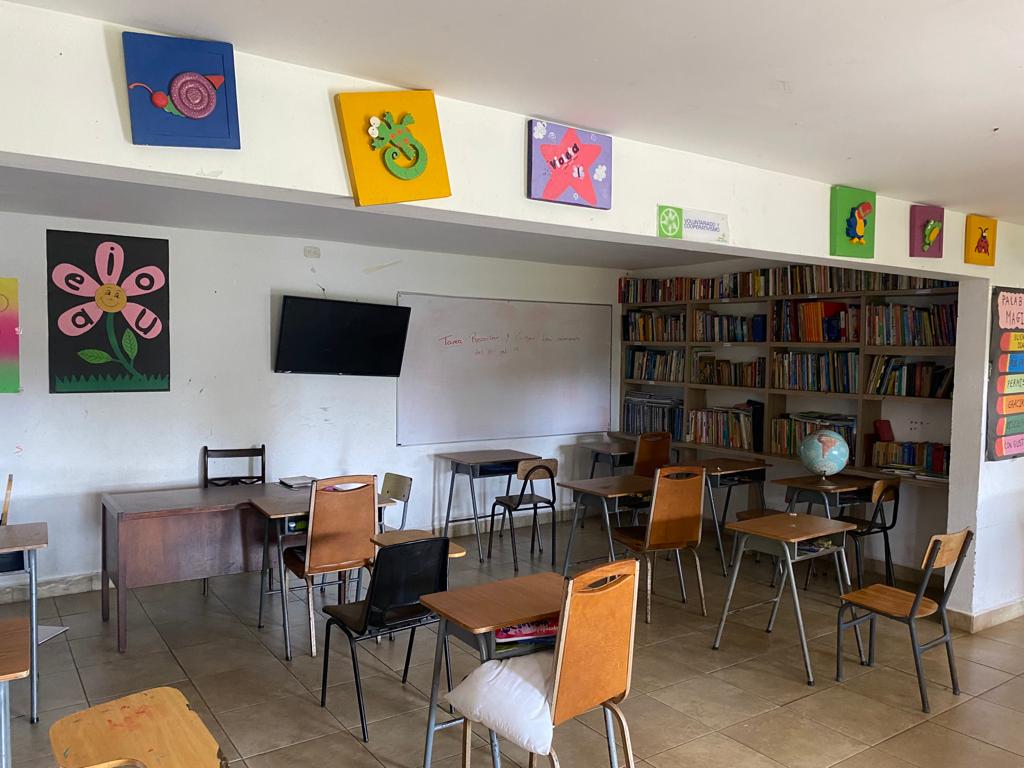 Salón con pupitres, tablero, decoraciones coloridas en la pared y una biblioteca