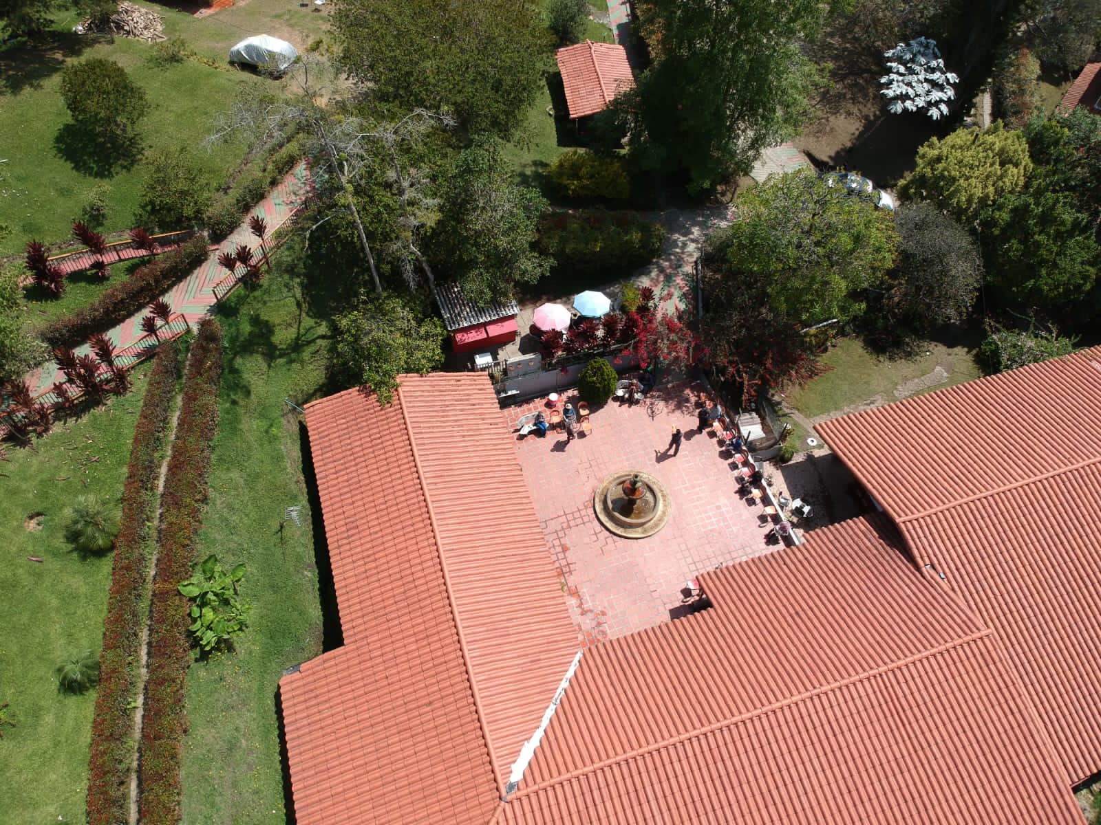 Vista aérea de un patio empedrado con una fuente, rodeado por los techos de teja del hogar y con personas sentadas