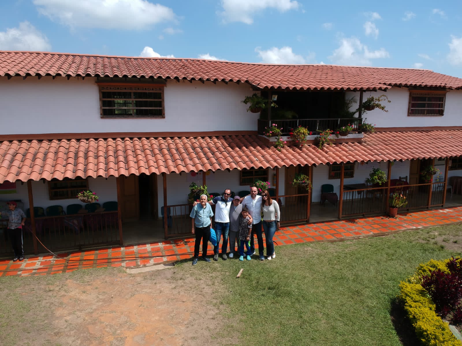 Grupo de personas posando frente al edificio de dos pisos, con corredor y macetas de flores