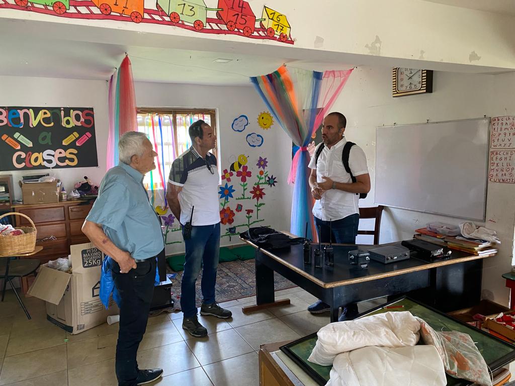 Salón decorado con dibujos infantiles y un cartel de «Bienvenidos a clases», donde tres personas conversan